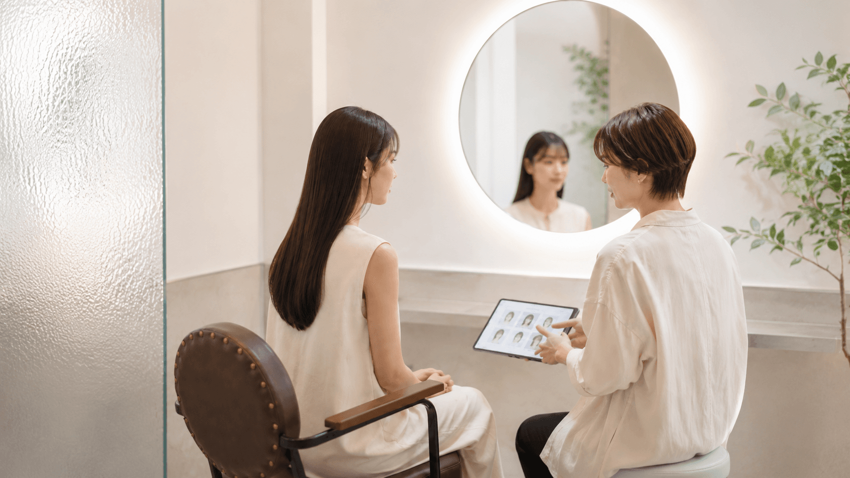鏡越しに向き合い、タブレットの髪質サンプルを見せながら丁寧にカウンセリングを行うスタイリストと女性